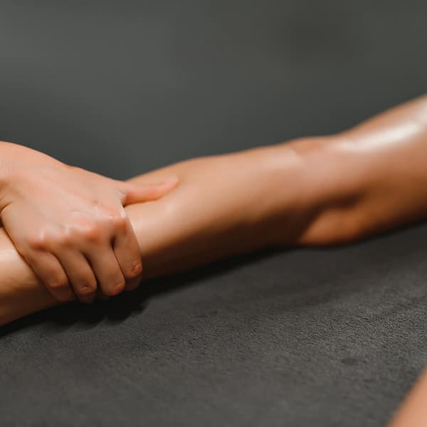 Hands gently holding and stretching a person's forearm during massage therapy on a gray surface.