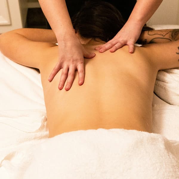 Person receiving a back massage on a white towel-covered table with tattooed arm visible.
