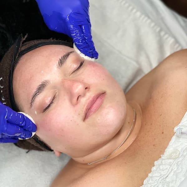Gloved hands providing a facial treatment to a person with their eyes closed