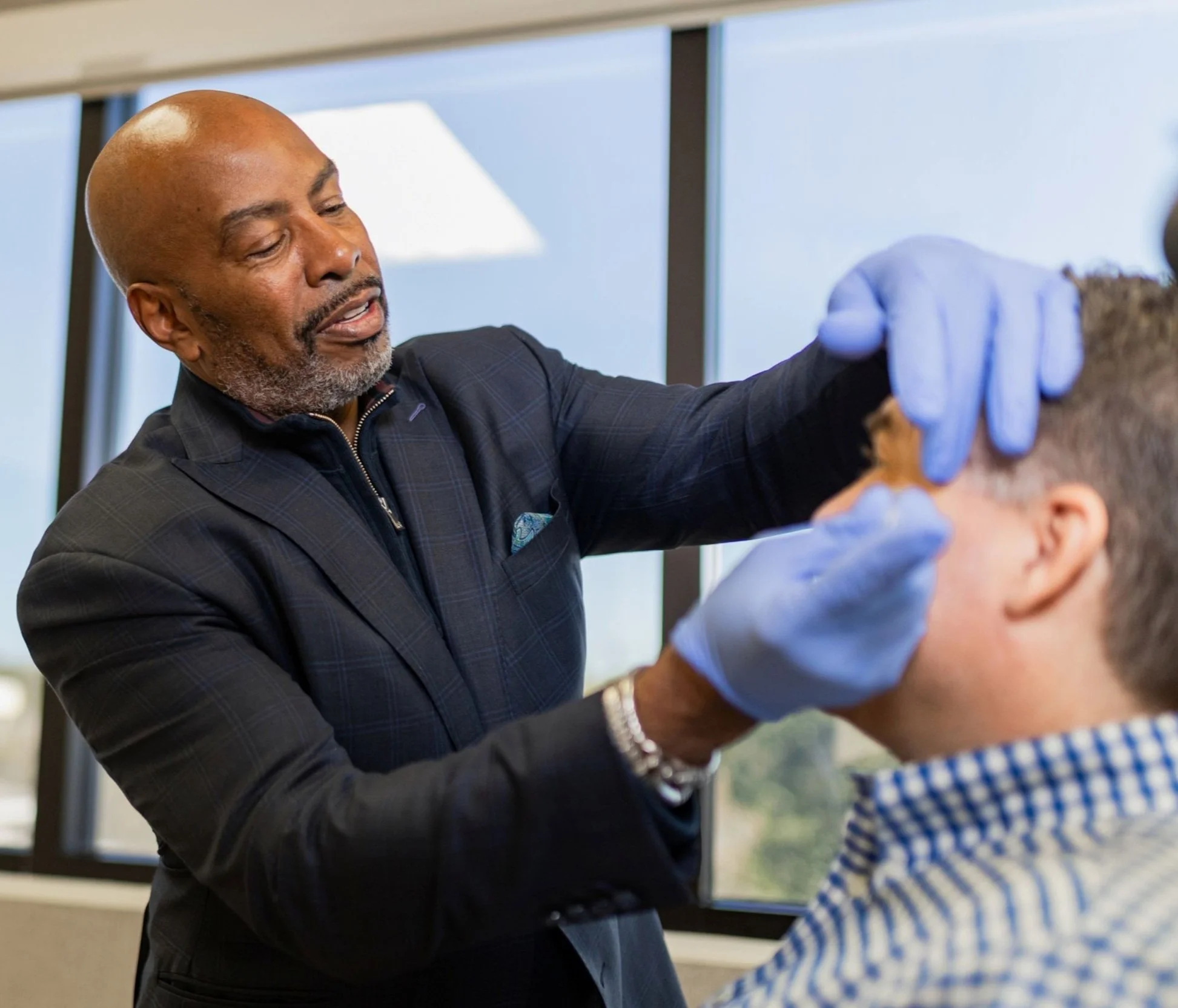 A doctor wearing blue gloves examines a man's face near his temple.